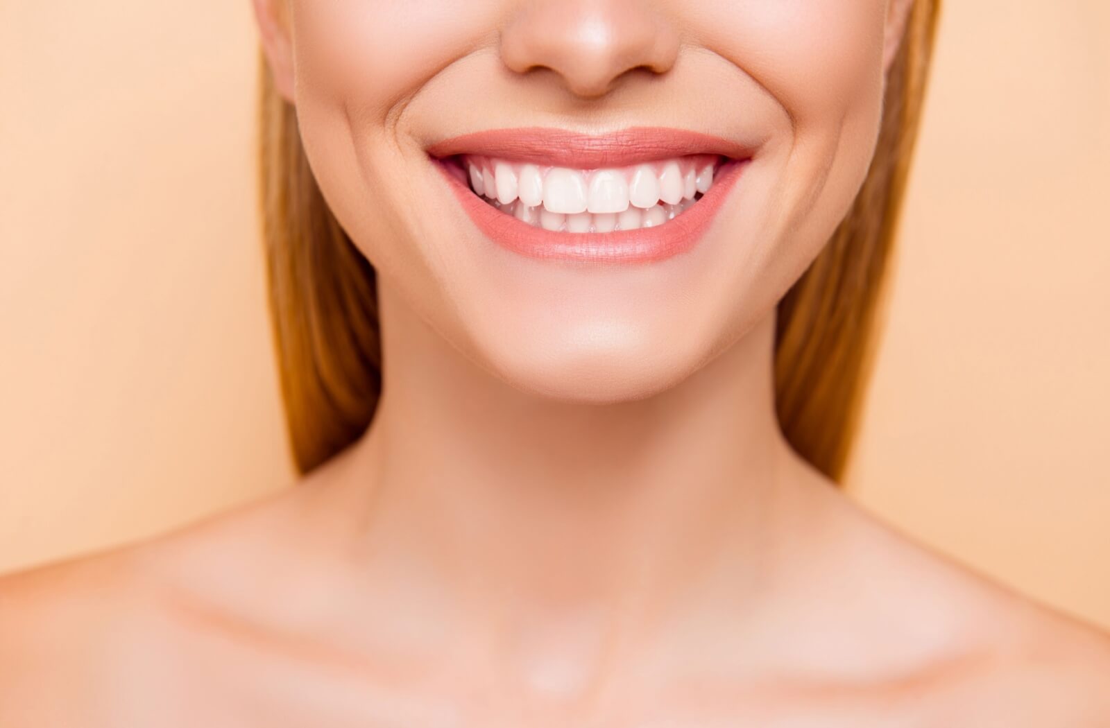 Close-up of a person smiling with bright white teeth against a peach background showcasing dental health and confidence.